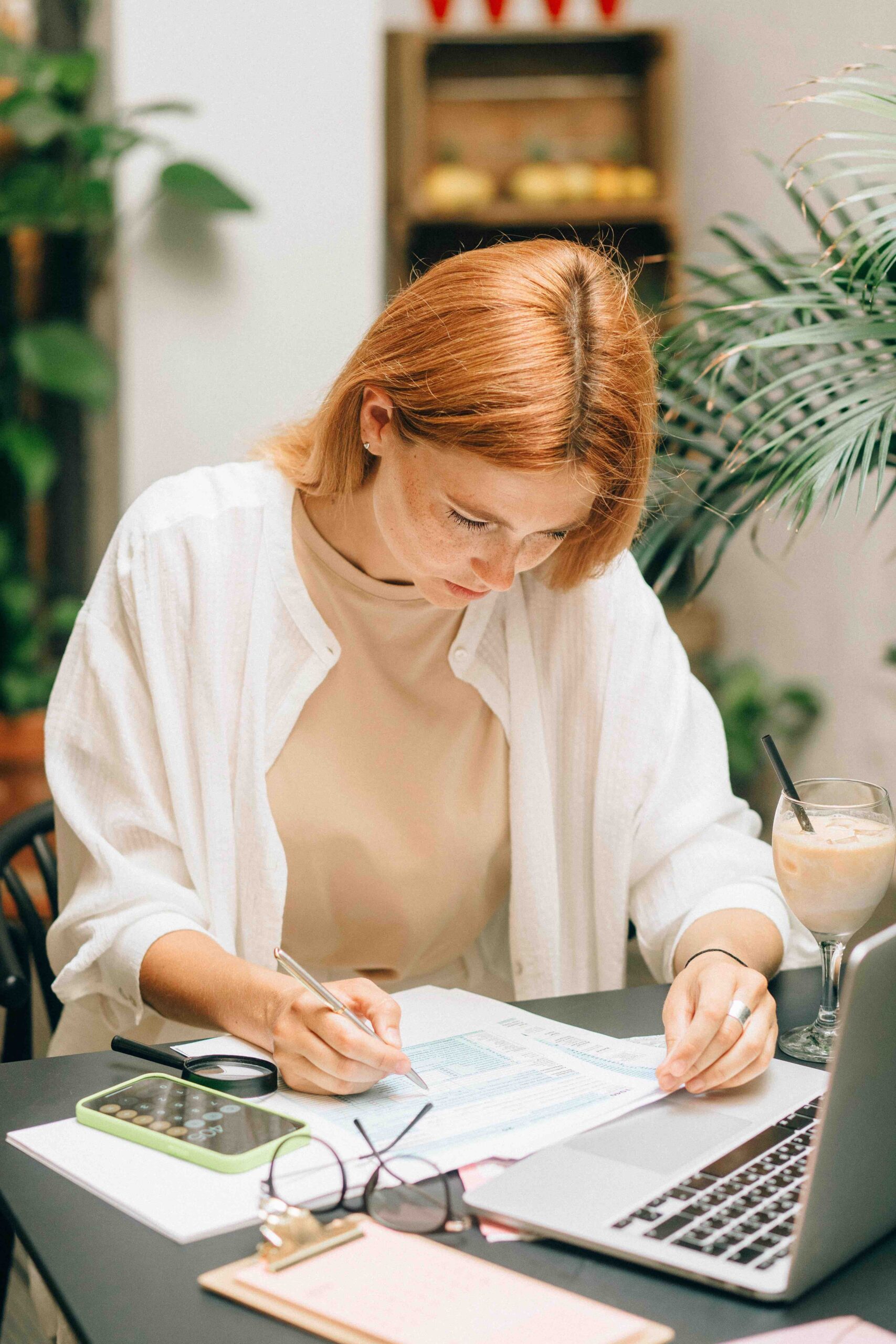 get invoices paid on time Business woman sitting at her desk, in front of her laptop and going through a list of unpaid invoices with a highlighter pen
